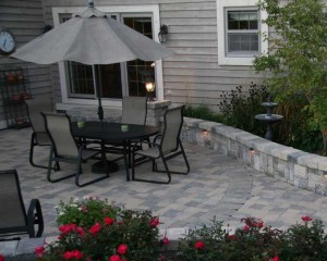 The perimeter of the main gathering space in the patio is defined by a circular paver band using the Brussels Block XL unit. The perimeter of the patio is adorned with shrub roses to add vibrant color and a bird bath to promote bird watching while enjoying the space.