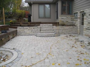 During Construction: The backyard patio space required the failing lannon stone retaining wall to be re-built while integrating a more user friendly staircase. The lannon park steps were installed at a greater rise to run ratio in order to reduce the steepness of the steps. The stairs feature a custom arc cut bottom landing that extends into the patio space to create a sense of arrival and add architectural detail.