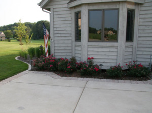 The improvements to the driveway entry area are dramatic. The existing concrete was saw cut to allow room for foundation plantings to enhance the entry area. The concrete is accented with a Brussels Block XL paver border course. Landscape path lighting amongst the ornamental plantings is incorporated to enhance driveway edge visibility and accent the house front entry.