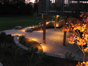 Nightscaping the lower patio with a warm glow allows the Owners to entertain at night or simply enjoy a pleasant view from the window. The landscape lighting includes a hidden light mounted under the deck joists to illuminate the patio from above permitting outdoor dining at night. Path lights frame and enclose the patio space. The face of the segmental retaining wall in the background is washed with a broad beam flood light.